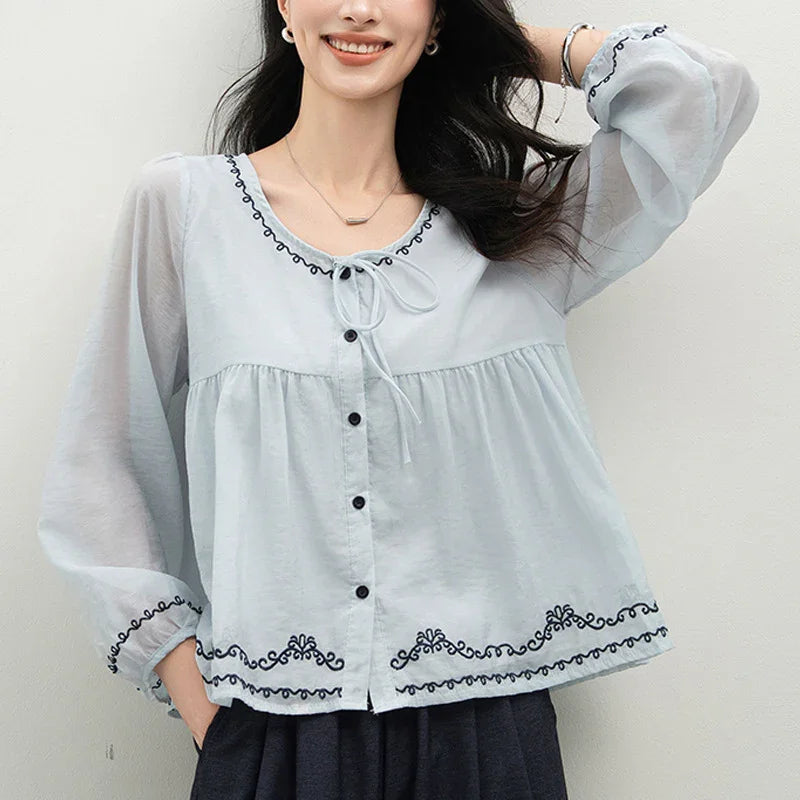 Woman wearing light blue long sleeve blouse with black embroidery and button front
