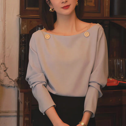 Woman wearing elegant light blue blouse with gold chain details and black skirt indoors