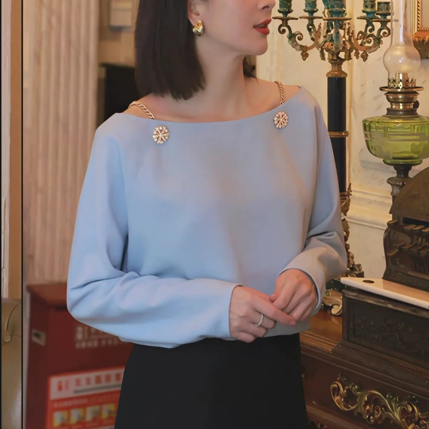 Woman in light blue chain-strap blouse with decorative buttons, elegant indoor setting